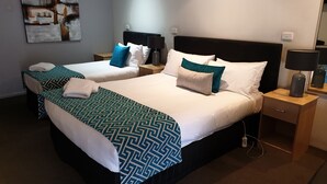 A hotel room with two beds, each with a patterned bedspread, white pillows, and a nightstand with a lamp. - Tenterfield Tavern and Motor Inn (Tenterfield)