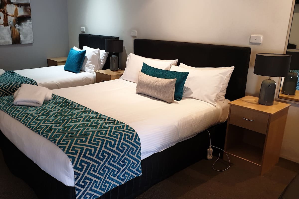 Habitación de hotel con dos camas, cada una con una colcha estampada, almohadas blancas y una mesita de noche con lámpara.