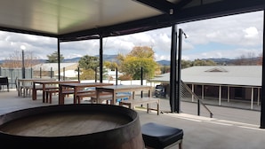 A spacious outdoor area with a wooden barrel, tables, and benches, offering a view of a building and mountains in the distance. - Tenterfield Tavern and Motor Inn (Tenterfield)