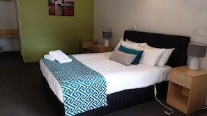 A neatly made bed with a patterned bedspread, a bedside table with a lamp, and a wall-mounted light switch.