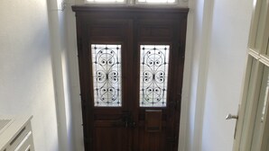 A wooden double door with decorative glass panels and a black doormat in front.