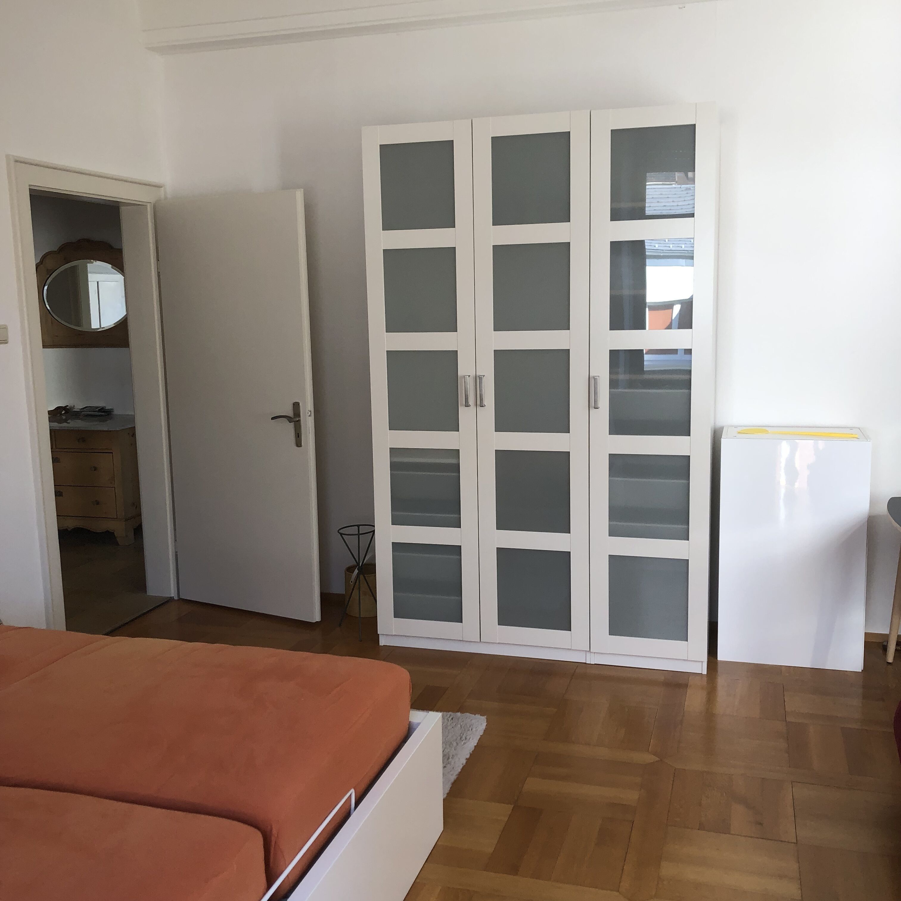 Makuuhuone, jossa on sänky, lasiovilla varustettu vaatekaappi, peili ja pieni pöytä.