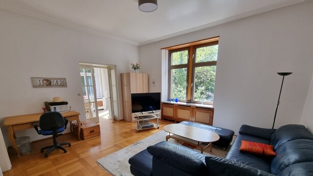 A living room with a blue sofa, a wooden coffee table, a TV, and a desk with a chair.