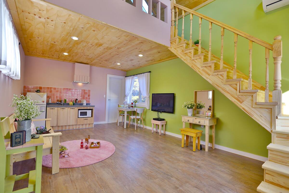 Un vaste espace de vie agrémenté d’un escalier en bois, une cuisine avec des meubles en bois et un coin repas avec un tapis rose.