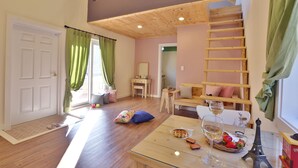 Una habitación acogedora con piso de madera, una mesa de vidrio con una cesta de fresas, una copa de vino y una pequeña réplica de la Torre Eiffel.