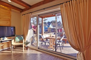 Een moderne woonkamer met een grote televisie, houten meubels en een schuifdeur naar een terras.