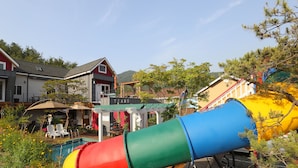 Un parque infantil con un tobogán colorido, una piscina y mesas para sentarse al aire libre.