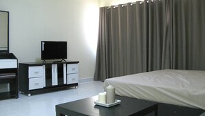 A hotel room with a bed, a TV on a dresser, a table with a candle, and a window with curtains. - T9 Muang Thong Thani Condo (Pak Kret)