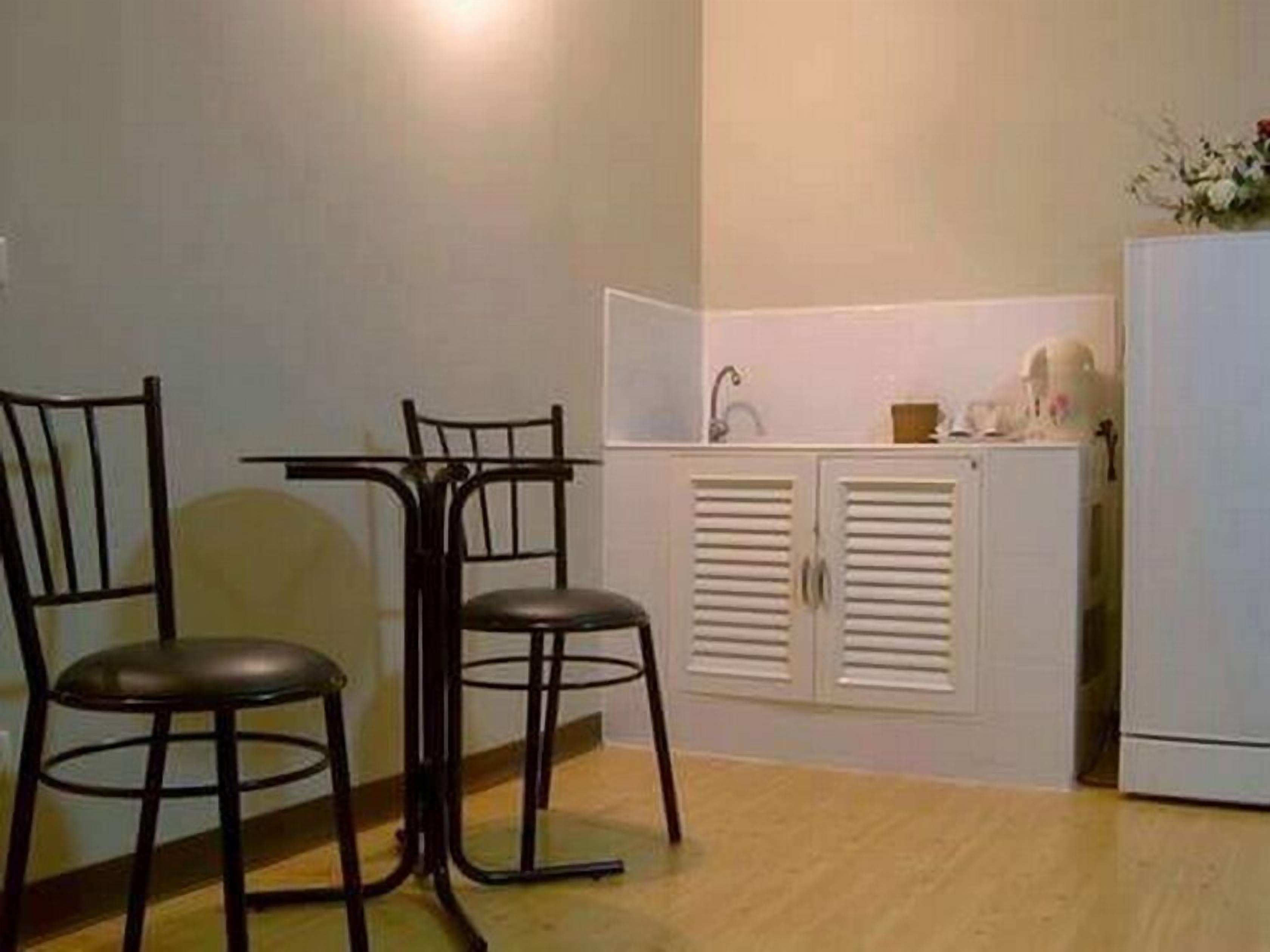 Een kleine kitchenette met een witte koelkast, een spoelbak en een aanrecht. Er staan twee zwarte stoelen en een tafeltje.