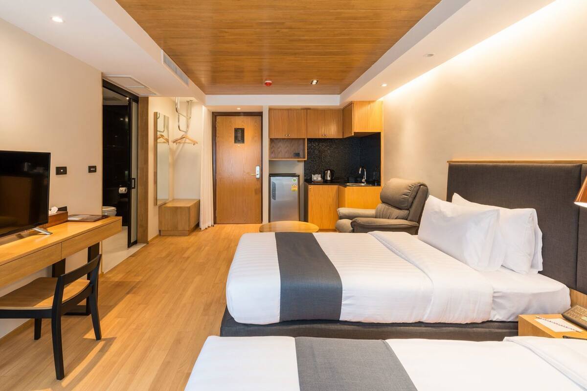 A hotel room with a bed, desk, TV, kitchenette, and a bathroom.
