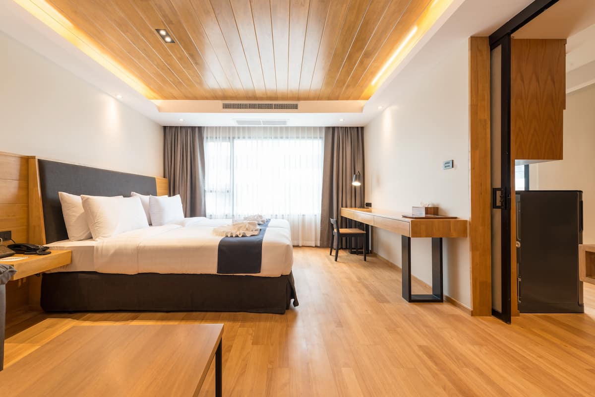 A modern hotel room with a wooden ceiling, a large bed with white linens, a desk, and a refrigerator.