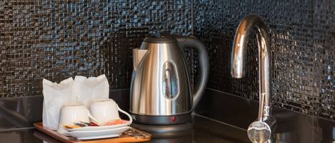 A modern kitchen with a stainless steel kettle, a sink, and a tray with cups and a plate of food.