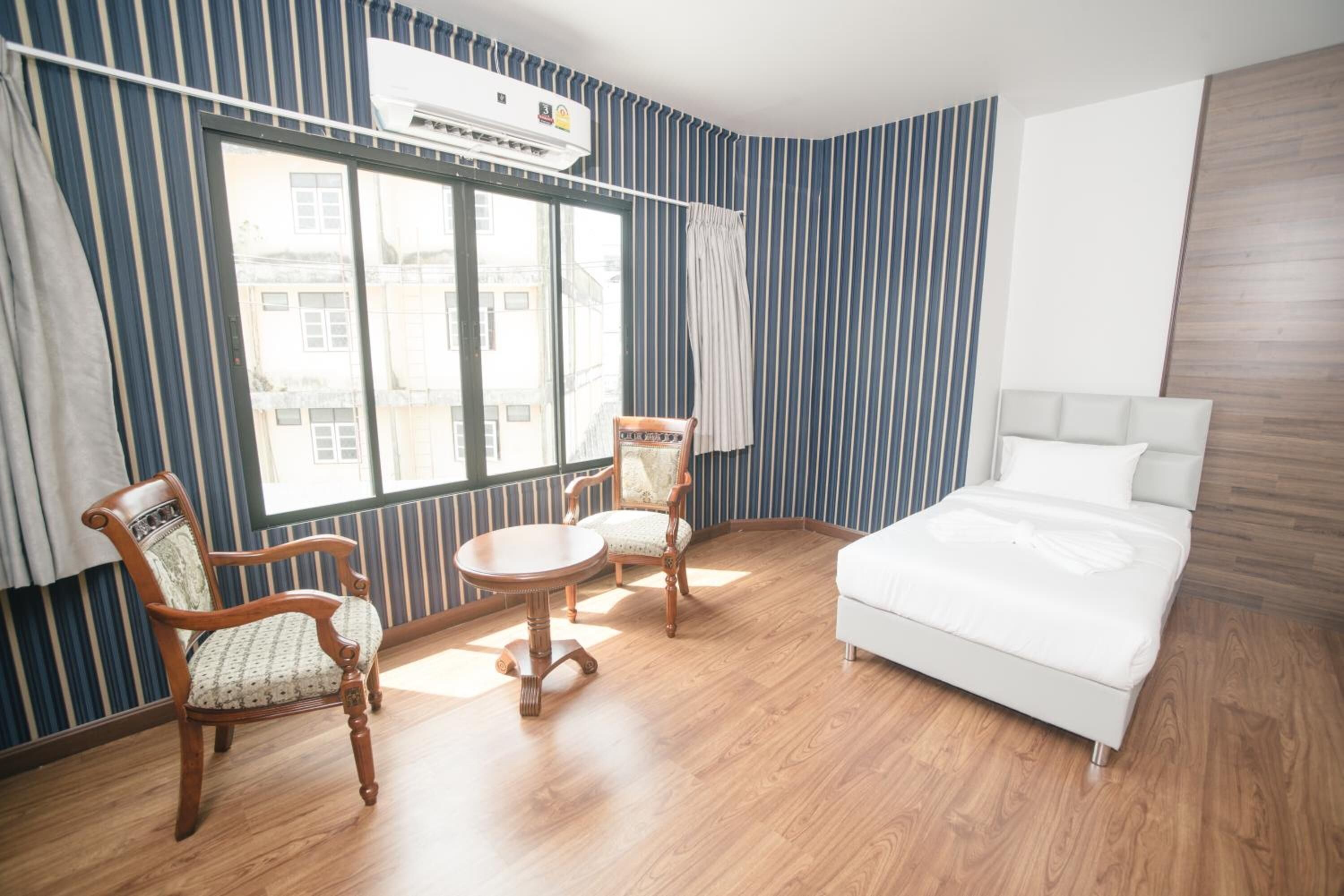 A hotel room with a bed, two chairs, a small table, and a large window with curtains.