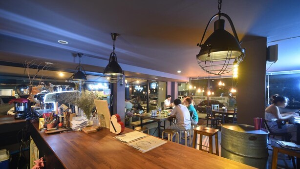 Un interior de restaurante con mesas de madera, lámparas colgantes y una zona de bar.