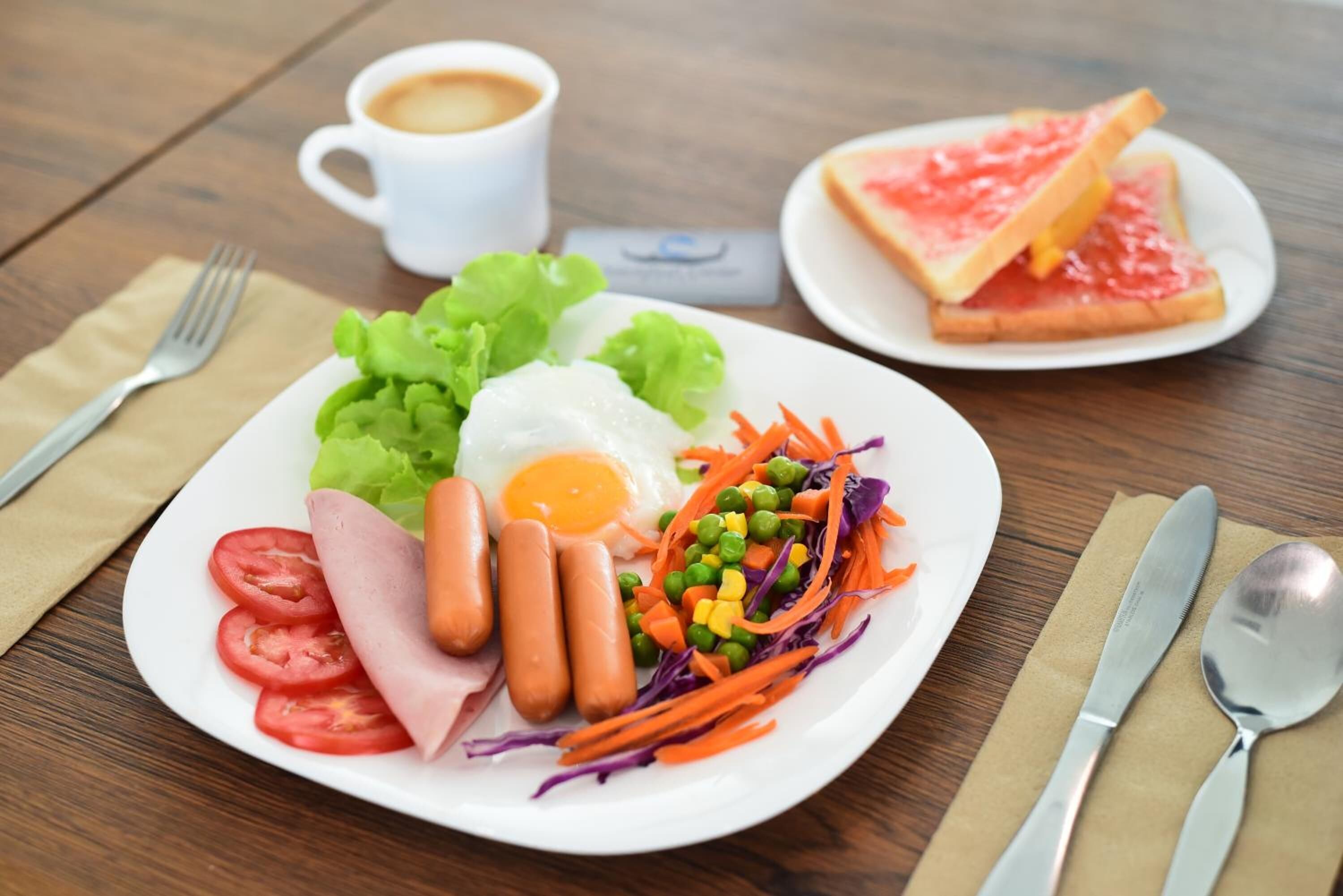 A plate of food with a cup of coffee, a fork, and a spoon on a wooden table.