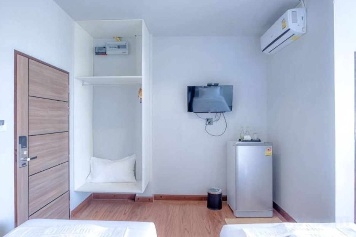 A room with a bed, a white wardrobe, a television mounted on the wall, and a small refrigerator.