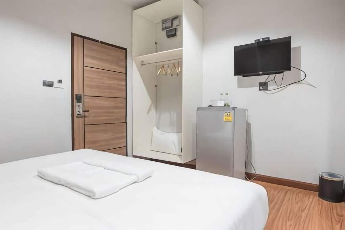 A hotel room with a bed, a wardrobe, a television, and a small refrigerator.