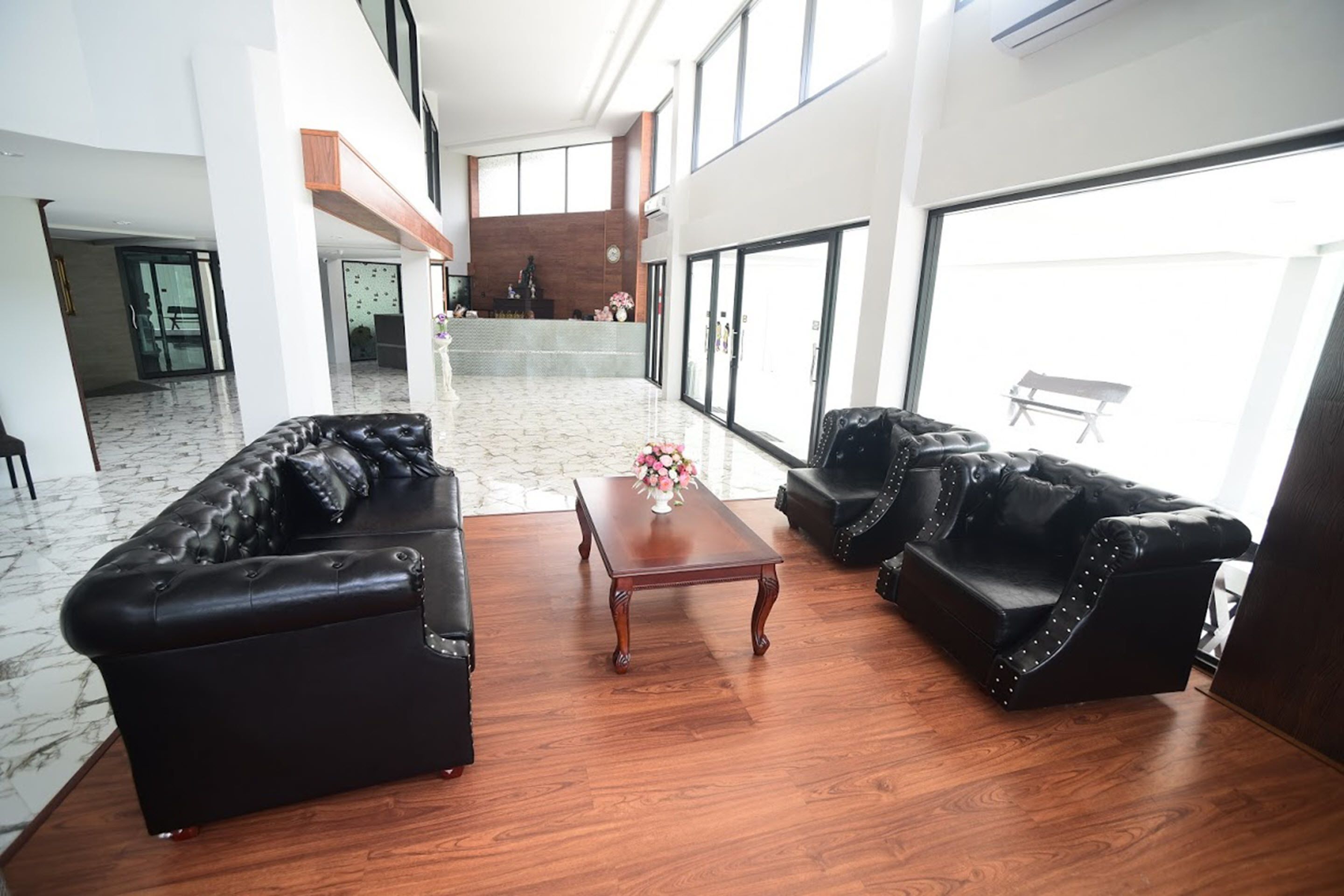 A spacious living area with two black leather sofas, a wooden coffee table, and a marble floor.
