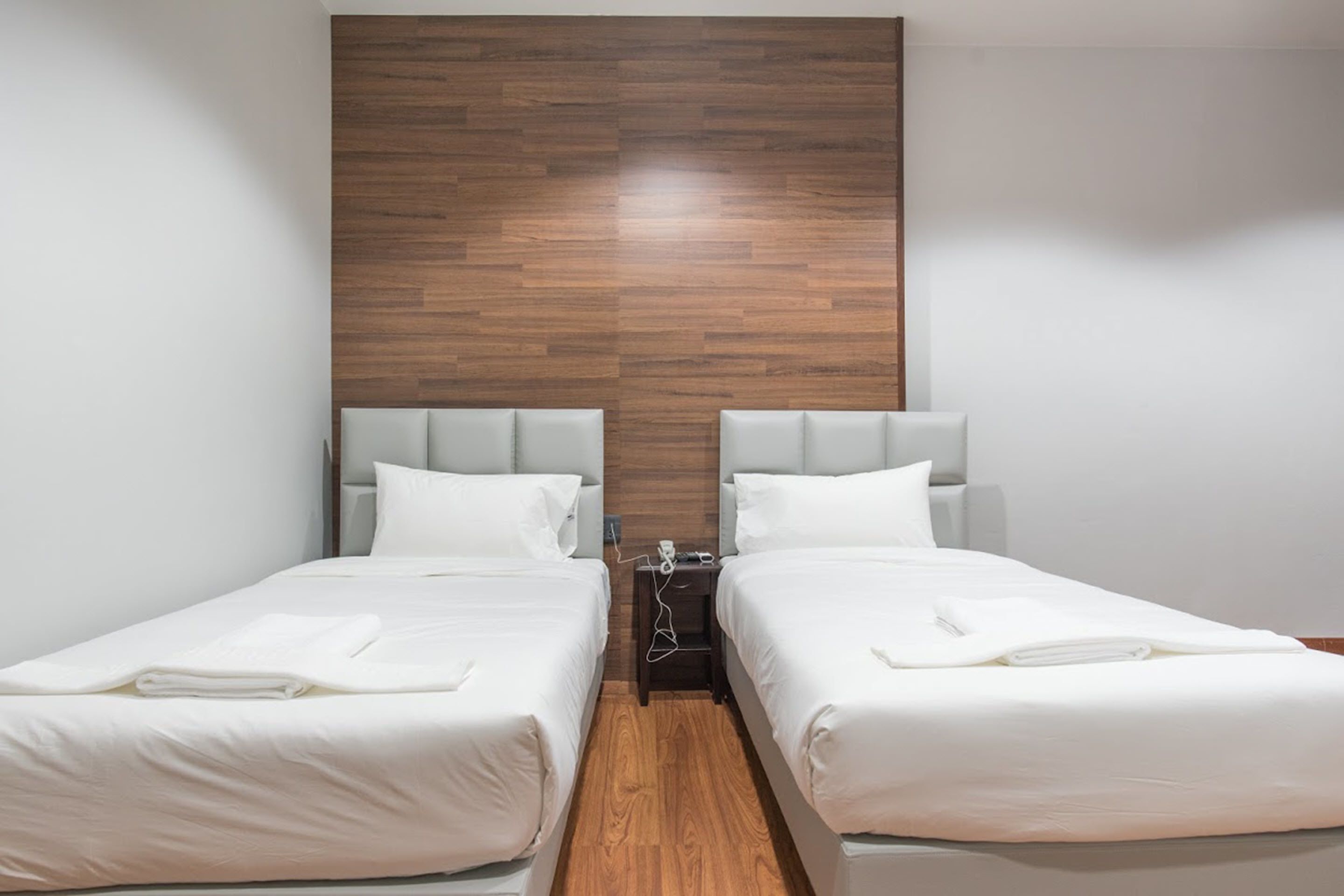 A hotel room with two single beds, a wooden accent wall, and a nightstand between them.