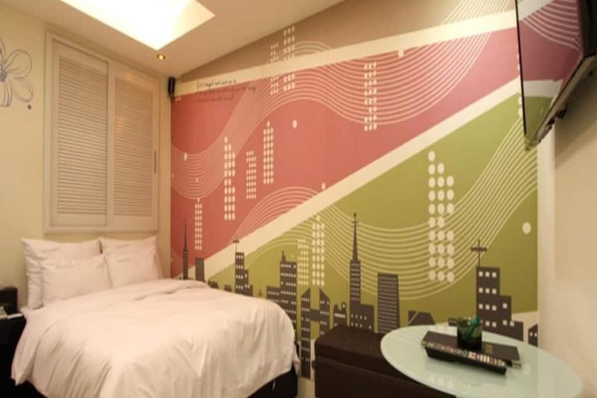 A hotel room with a bed, a round table, and a cityscape mural on the wall.