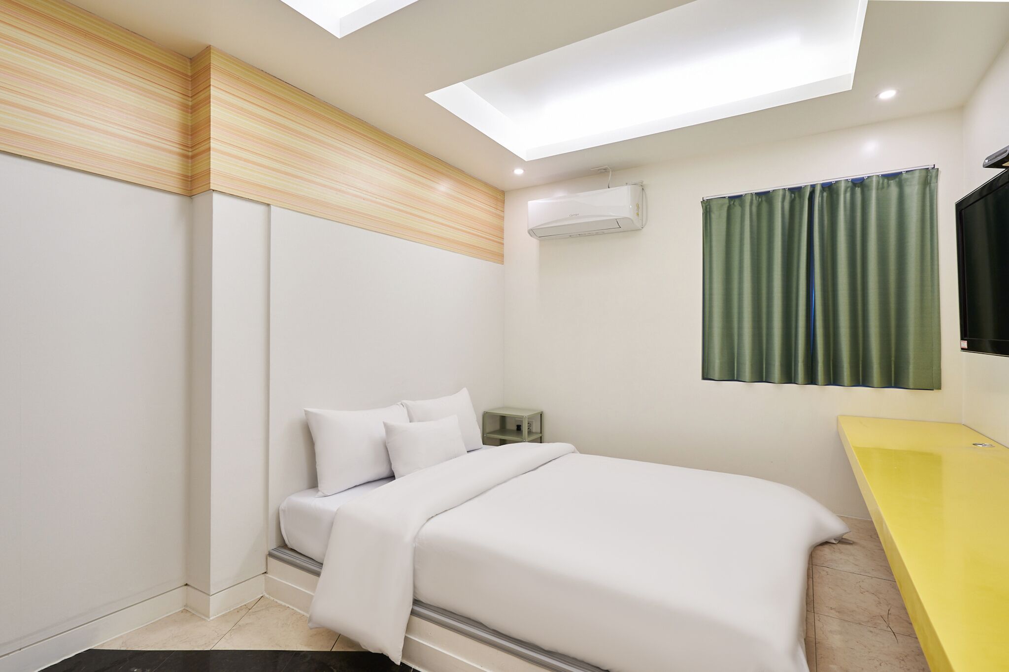 A modern bedroom with a bed, a yellow vanity, an air conditioning unit, and a green curtain.