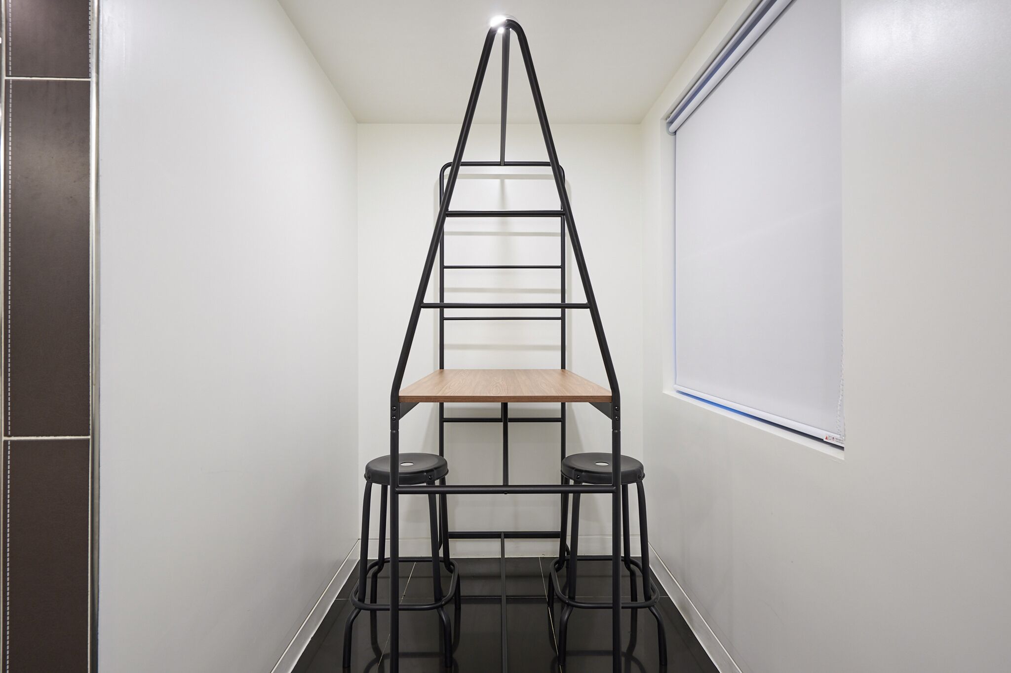 A black metal ladder shelf unit with a wooden top shelf and two black stools.