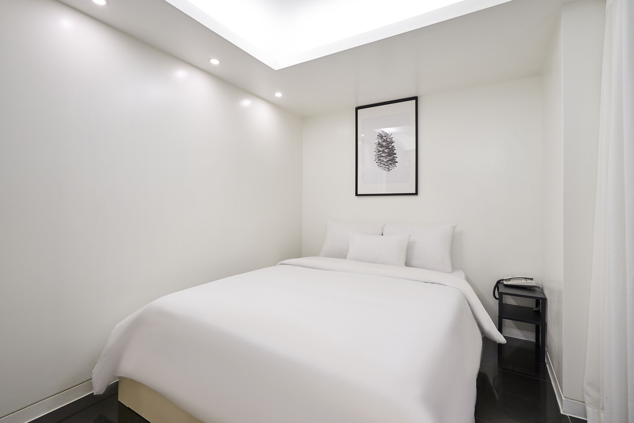 A modern hotel room with a large bed, a bedside table, and a framed artwork on the wall.