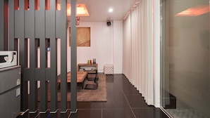 Una habitación de hotel moderna con una puerta corrediza, una zona de comedor con mesa y sillas, un microondas y un armario pequeño.