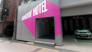 Entrada de un hotel con un cartel grande que dice "SHOW HOTEL" y un coche estacionado adentro.