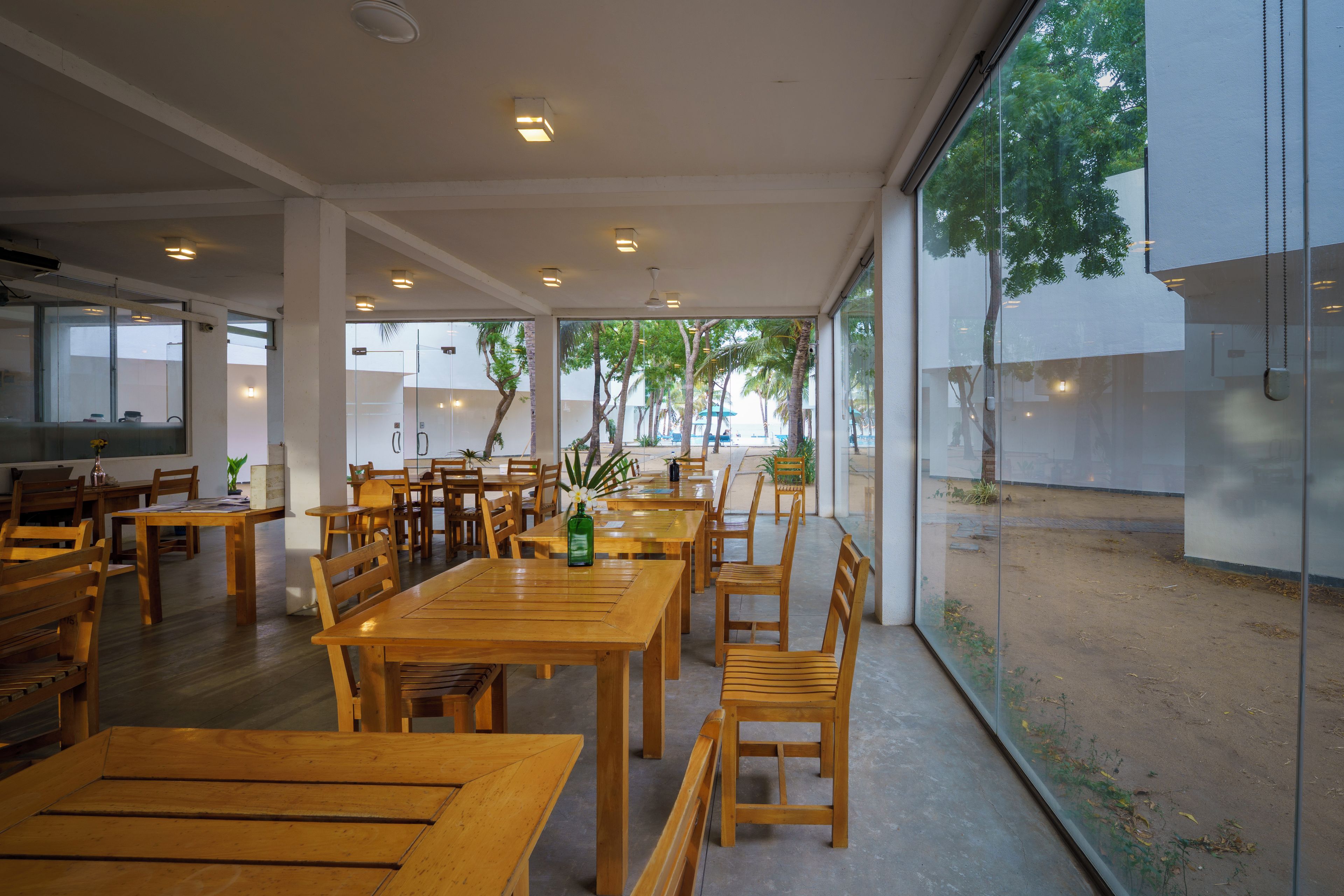 A spacious indoor dining area with wooden tables and chairs, large windows, and a view of the outdoors.
