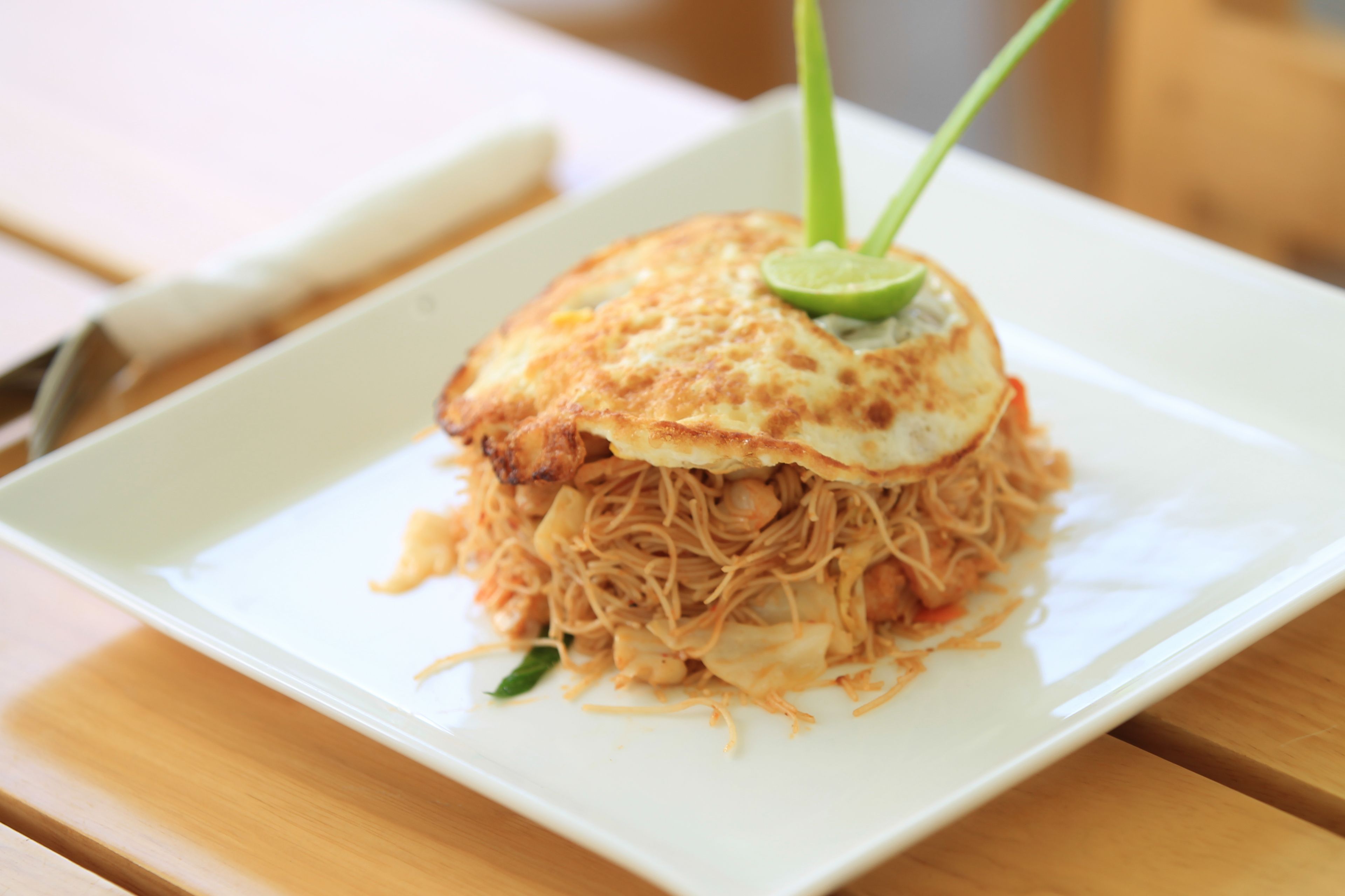 A plate of noodles topped with a fried egg and a slice of lime, served on a white plate.