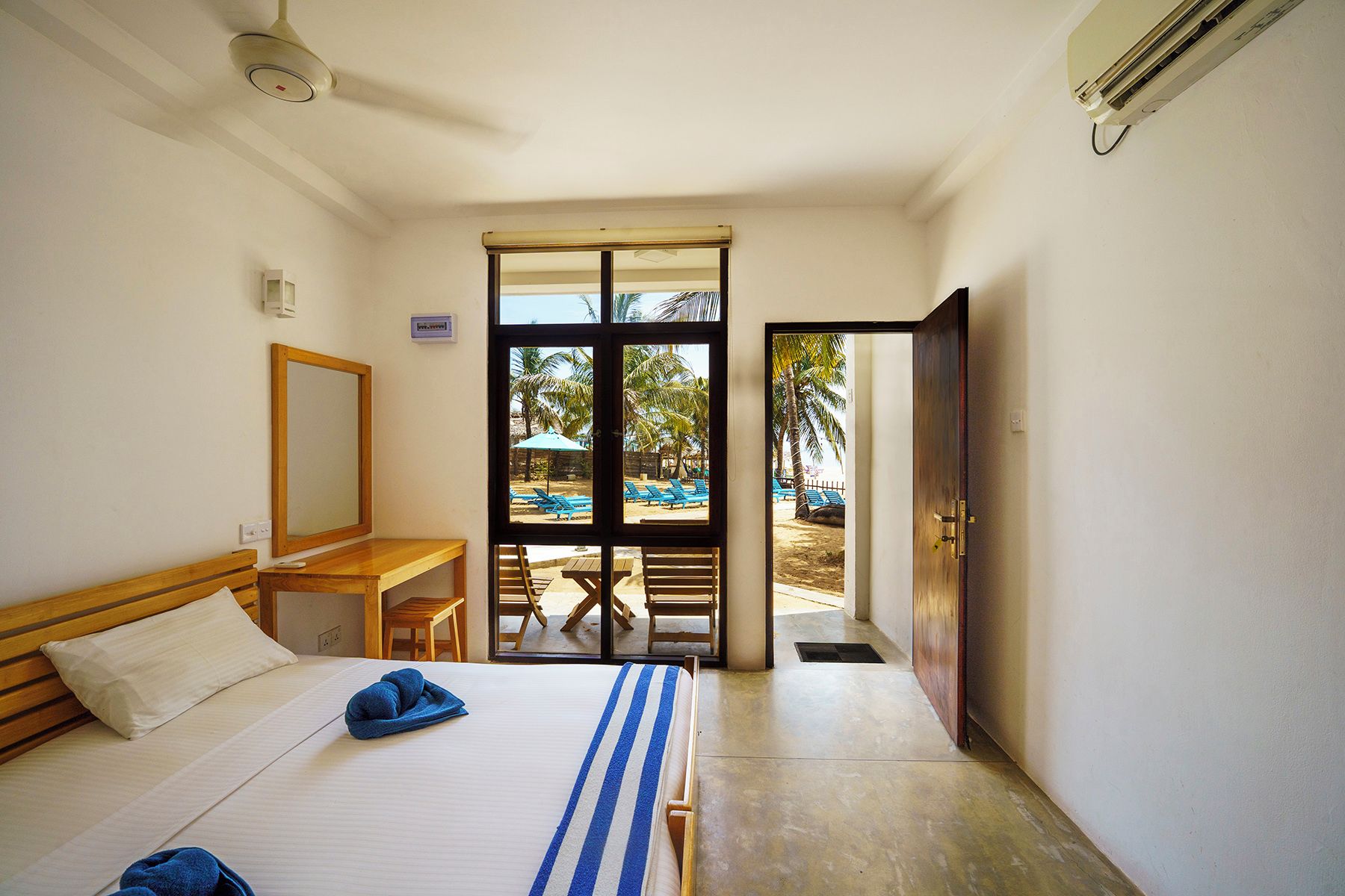 Habitación de hotel con cama, escritorio y vistas a un espacio exterior con sillas y sombrillas.