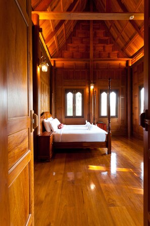 A wooden-floored bedroom with a large bed, two nightstands, and a window with a view.