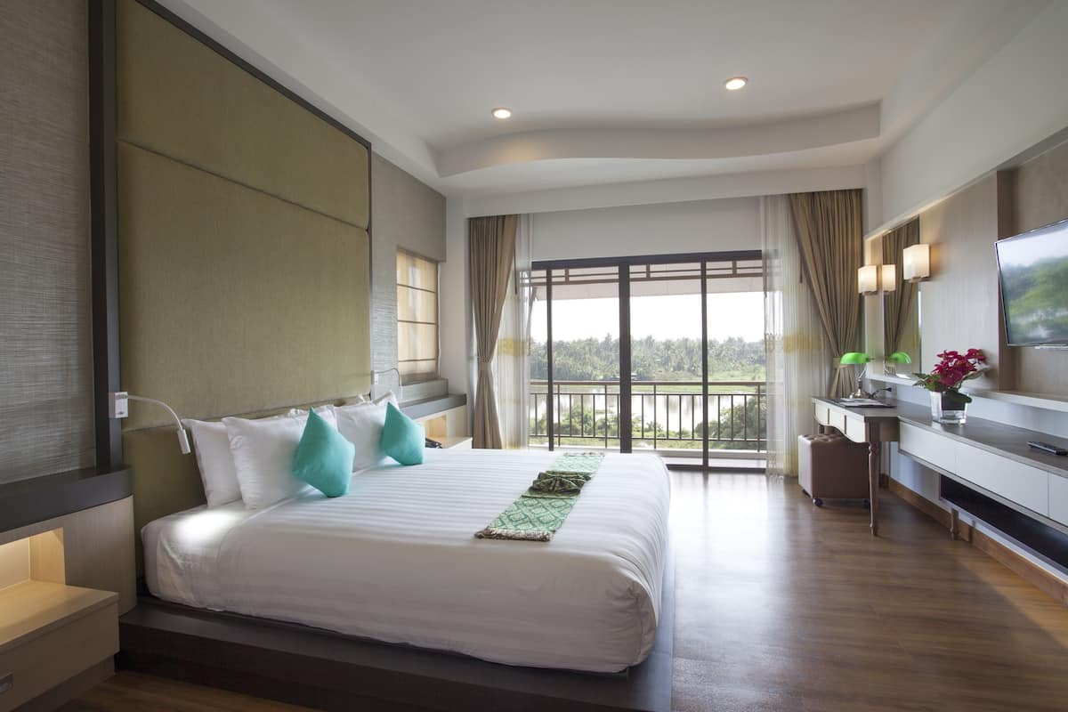 A modern hotel room with a large bed, a desk, a TV, and a balcony with a view.