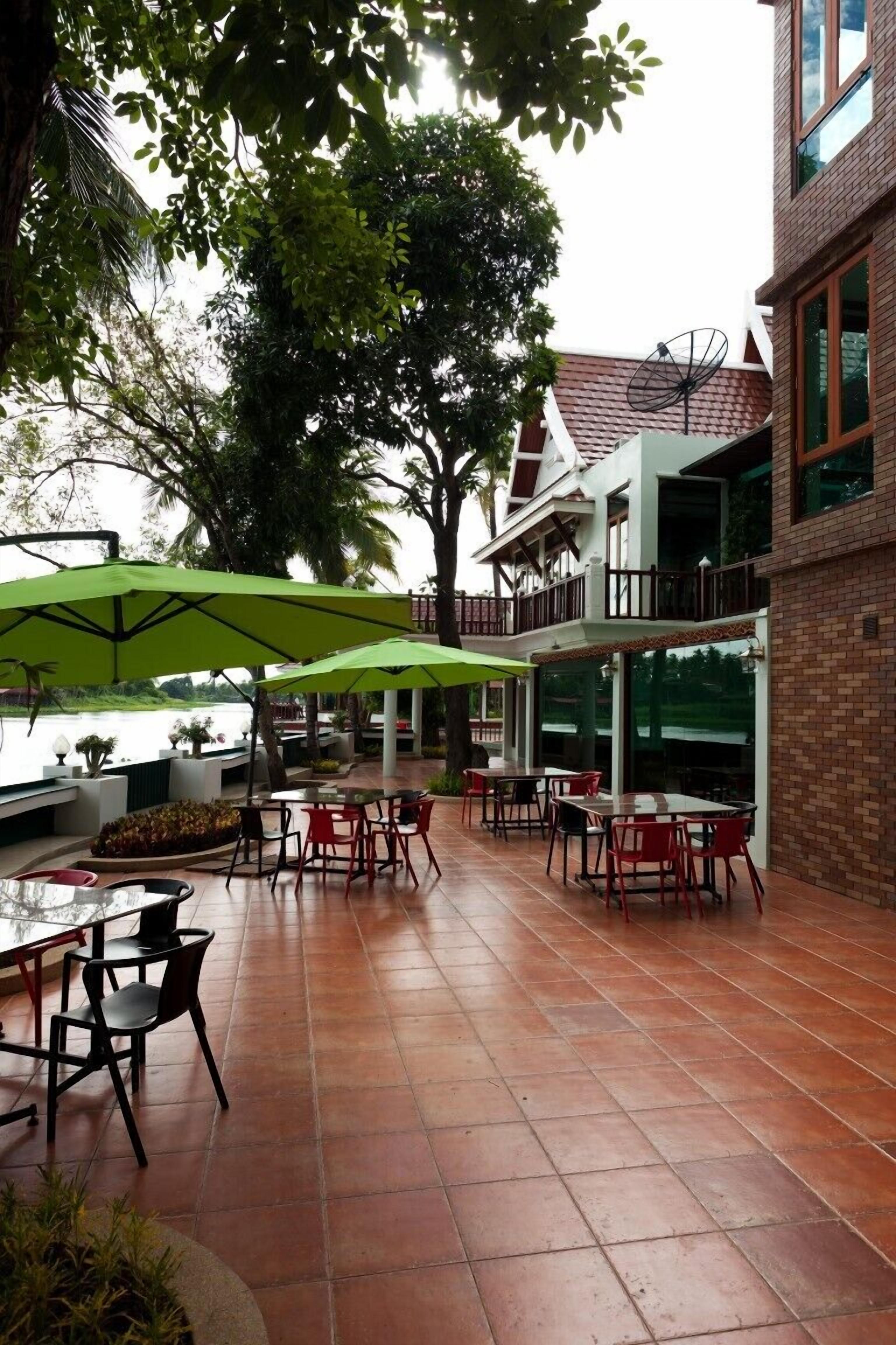 An outdoor patio area with tiled flooring, red and black chairs, and green umbrellas.