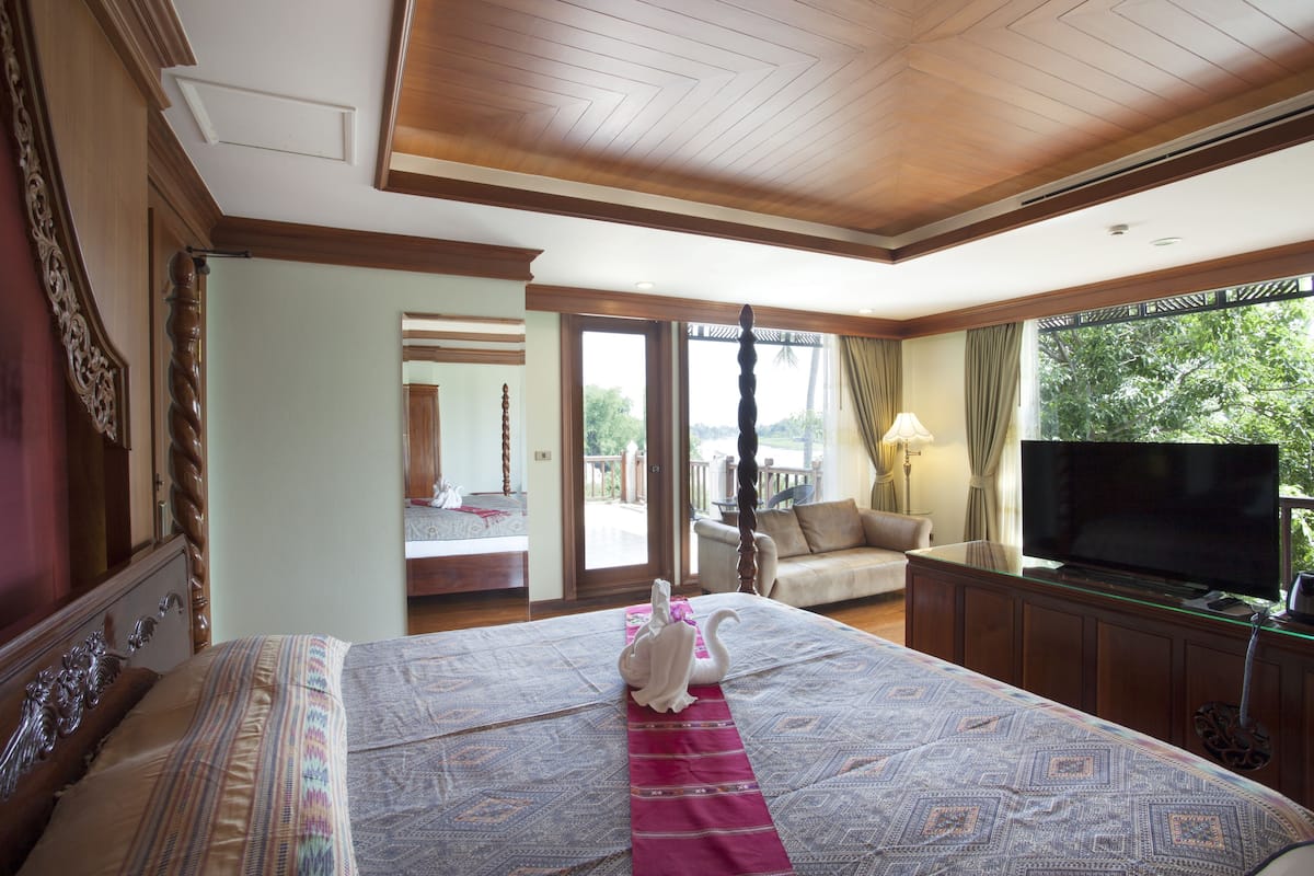 A hotel room with a large bed, a television, and a balcony with a view of trees.