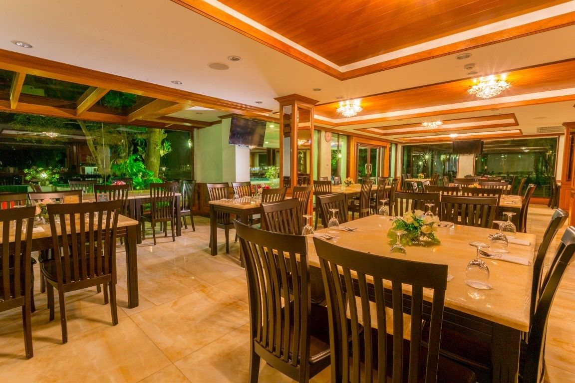 A restaurant with multiple dining tables and chairs, a wooden ceiling, and a view of greenery outside.