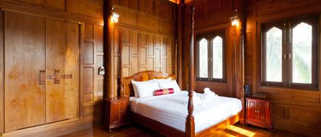 A large wooden four-poster bed with a white bedspread and red accents, flanked by nightstands and a small cabinet.