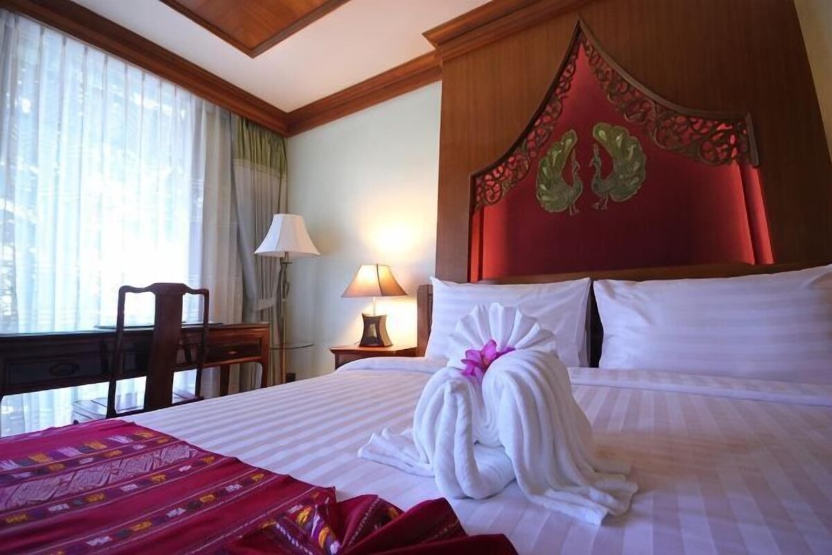 A hotel room with a bed, a desk, a chair, a lamp, and a window with curtains.