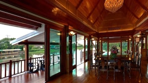 A spacious dining area with a large table and chairs, wooden paneling, and a chandelier. - RK Riverside Resort & Spa (Sam Phran)