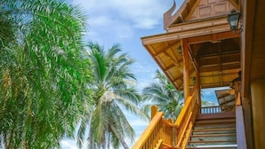 A wooden staircase leading to a traditional roofed structure surrounded by lush greenery and palm trees. - RK Riverside Resort & Spa (Sam Phran)