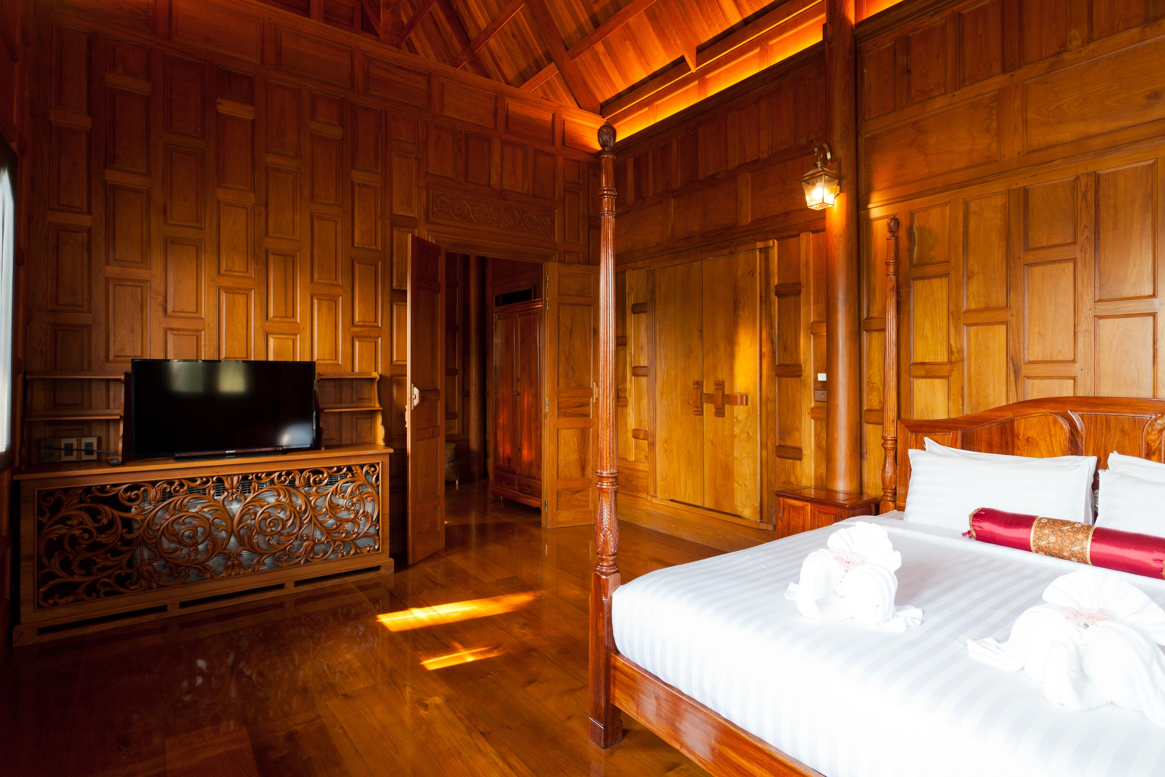 A wooden-paneled room with a bed, a TV on a stand, and a hallway leading to another room.
