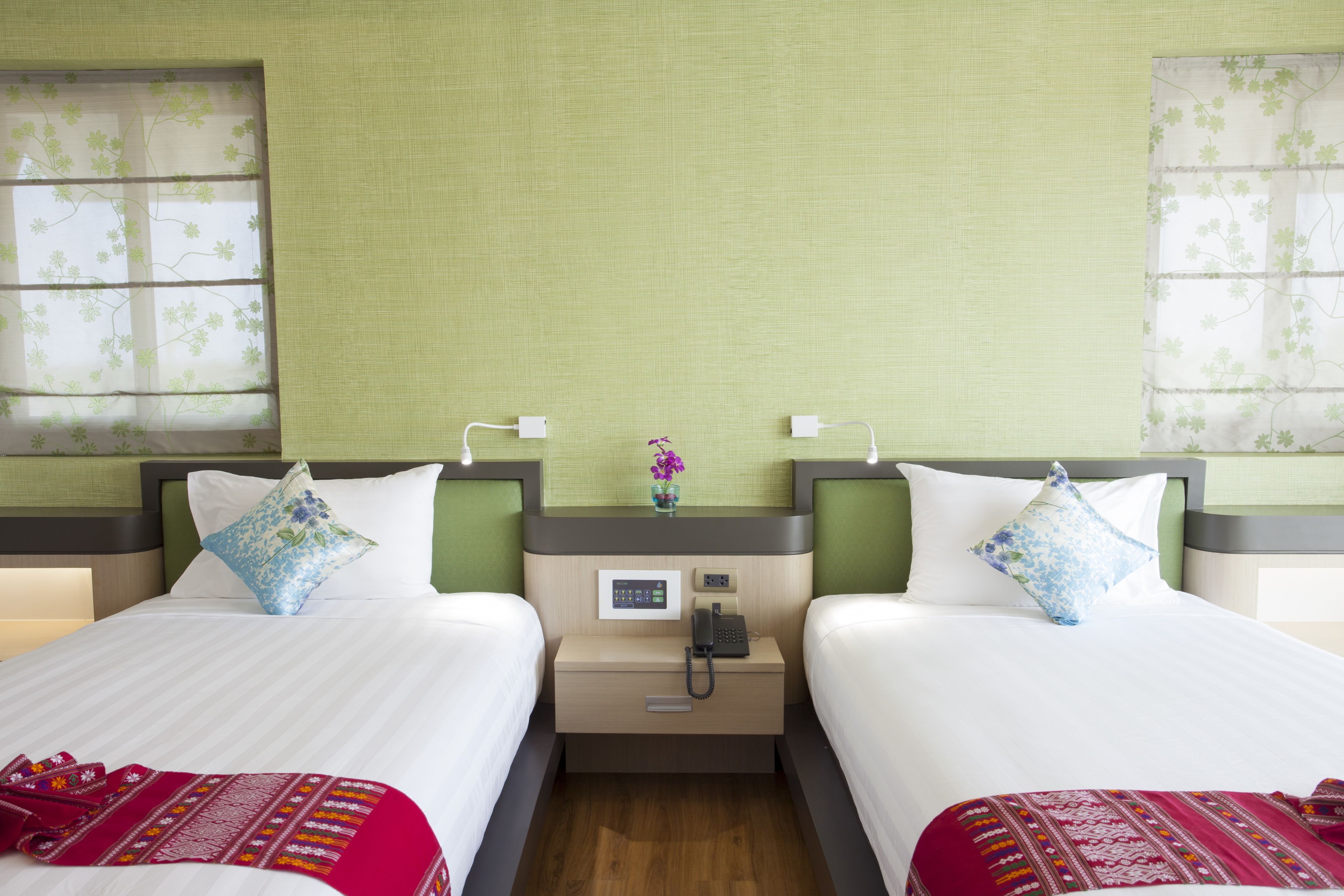 Habitación de hotel con dos camas, cada una con una almohada y una mesita de noche con teléfono y un pequeño jarrón.