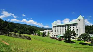 A large, multi-story building with a green roof, surrounded by a grassy area and trees.