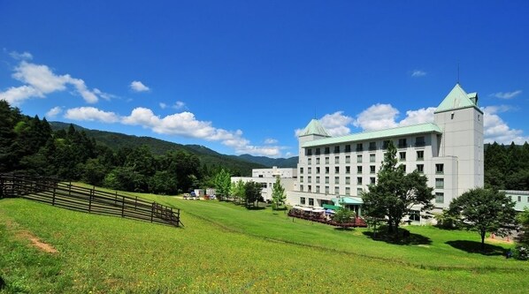 A large, multi-story building with a green roof, surrounded by a grassy area and trees.