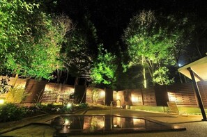 A nighttime outdoor area with a pool, wooden fences, and trees illuminated by artificial lighting. - Blue Ridge Hotel (Toyooka)
