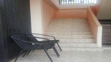 A staircase with a tiled floor leading to a higher level. There are two black metal chairs placed against a wall.