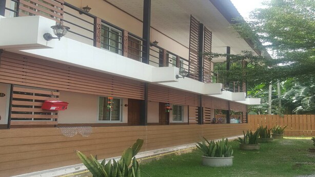 A two-story building with a flat roof, wooden slats on the ground floor, and a balcony on the upper floor. - Charlee House (Trang)