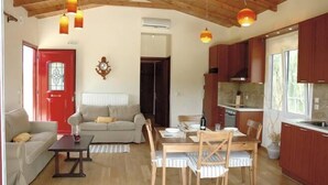 Una sala de estar acogedora con una puerta roja, un comedor con una mesa y sillas de madera, y una cocina con armarios de madera y un ventanal grande.