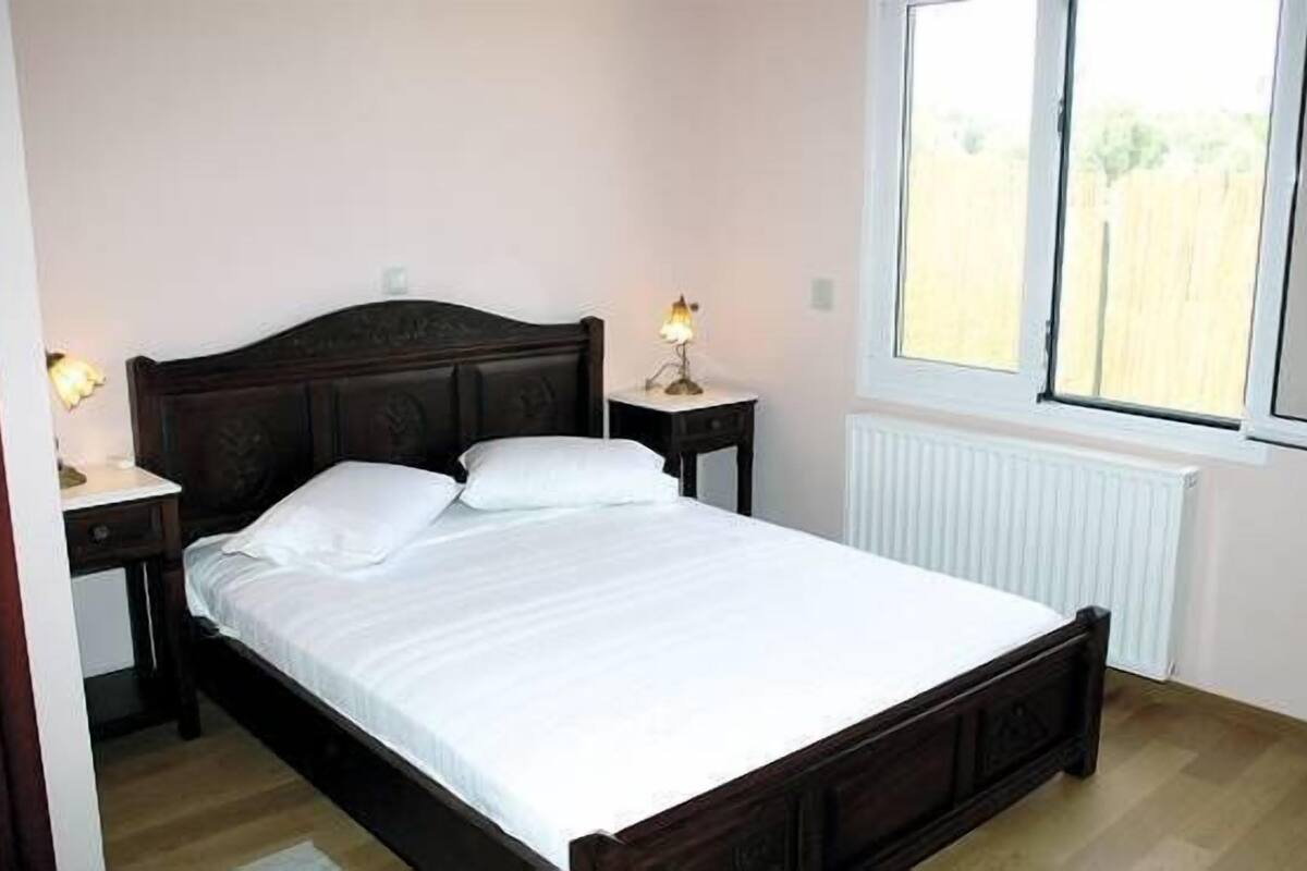 Une chambre à coucher avec un lit en bois, deux tables de chevet avec des lampes, une fenêtre et un radiateur.